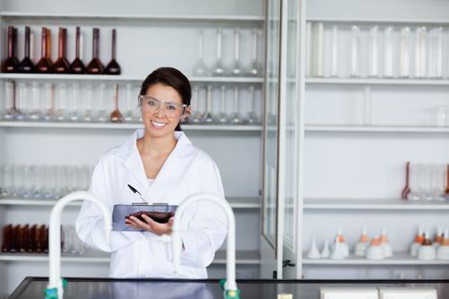 Smiling woman in laboratory writing on a clipboard.